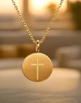 Gold necklace with a round pendant featuring a cross on a blurred background