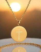 Gold necklace with a cross pendant against a warm background