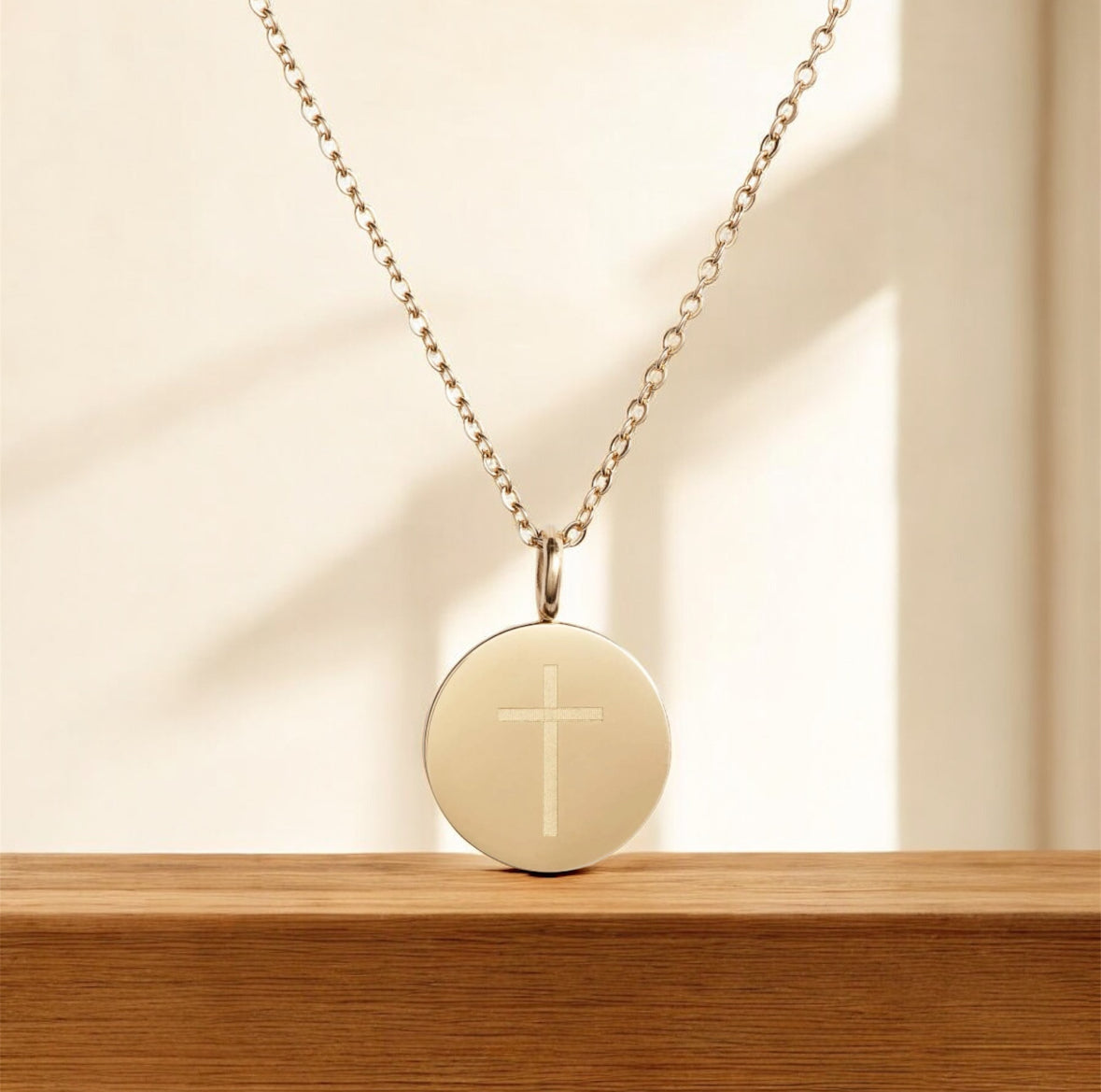 Gold necklace with a round pendant featuring a cross on a wooden surface.