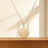Gold necklace with a round pendant featuring a cross on a wooden surface.