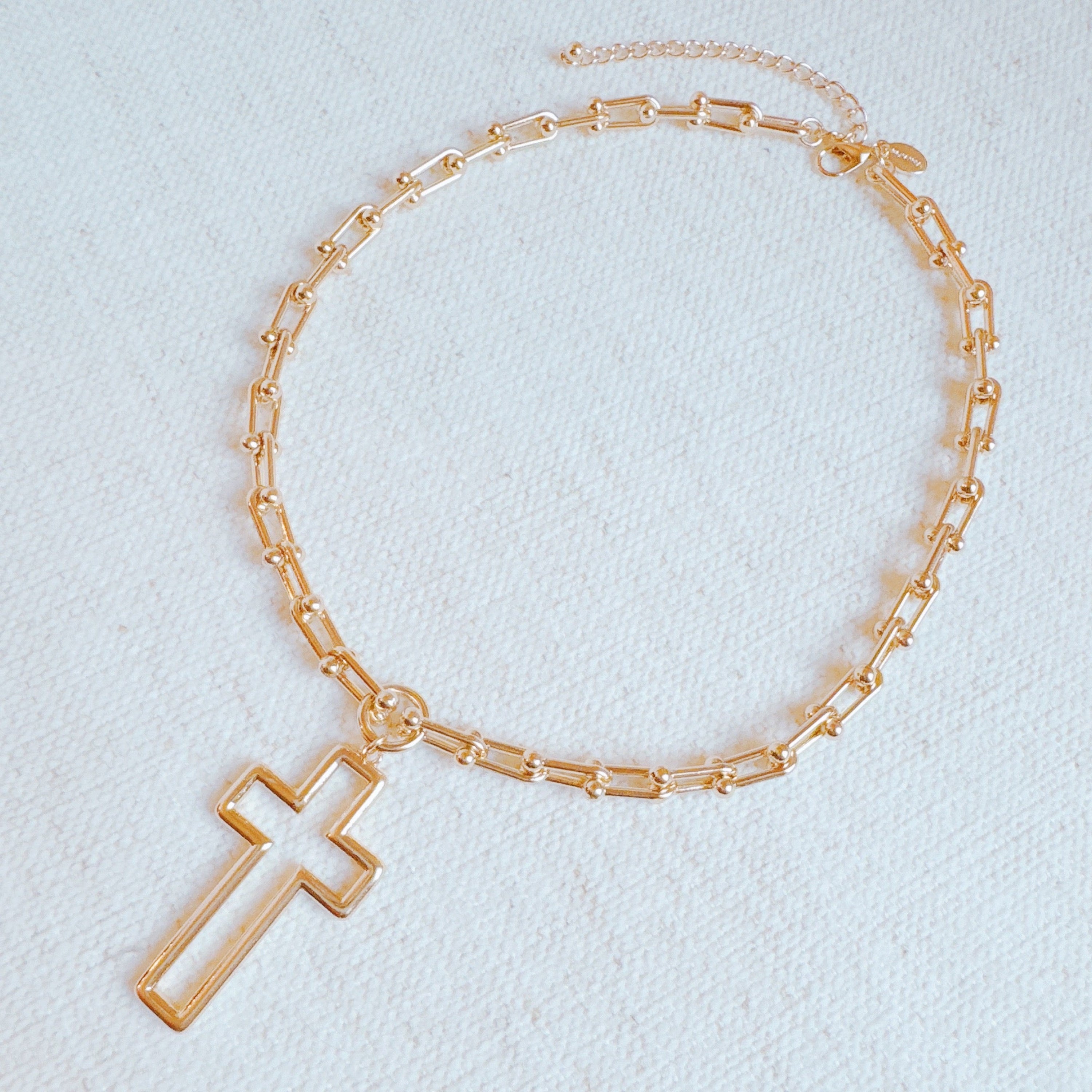 A gold cross pendant necklace on a U-shaped chain