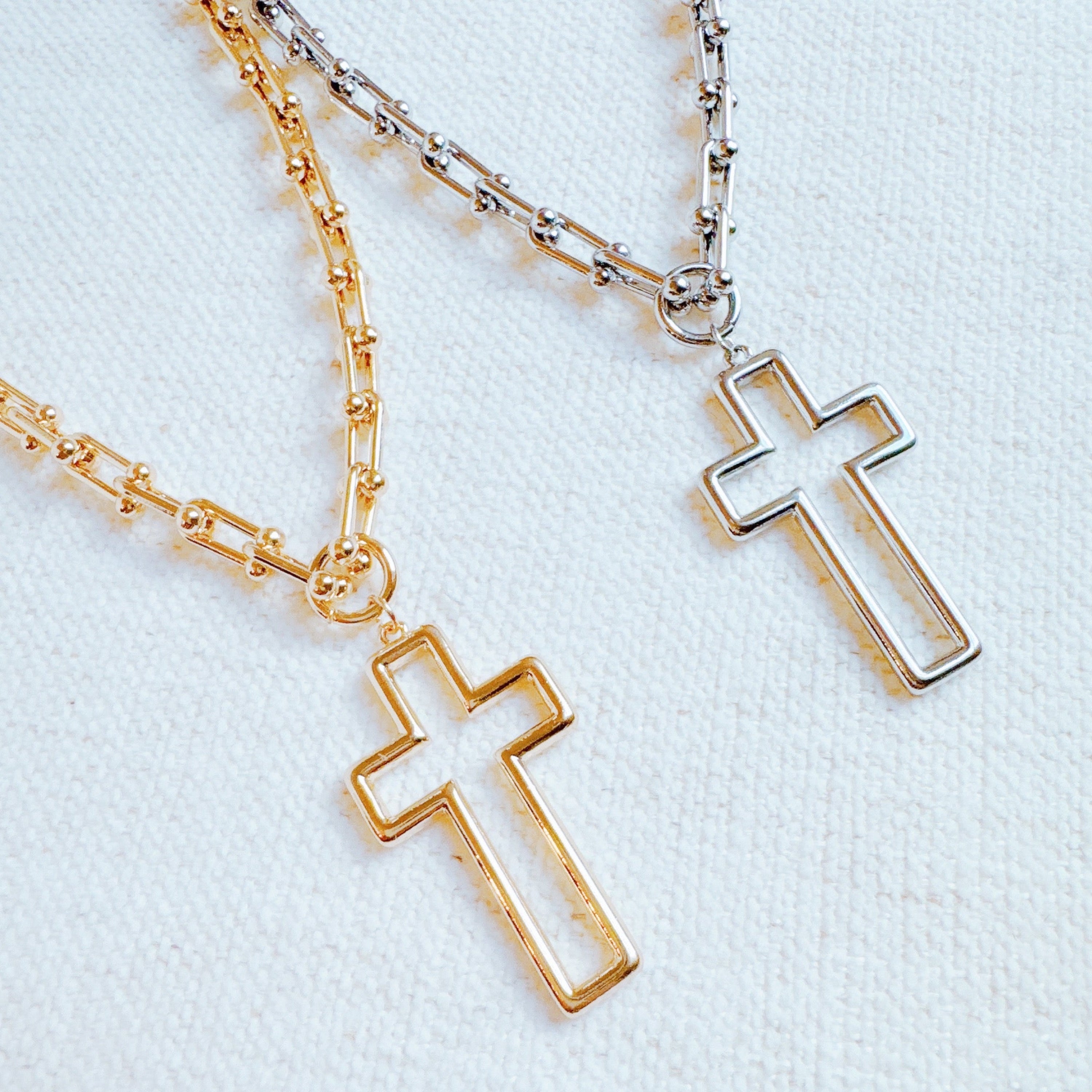 Two cross pendant necklaces on a U-shaped chain, one in gold color and one in silver, displayed against a white background.