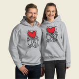 A man and woman wearing "Men Holding Heart Icon" hoodies, featuring a street art style graphic of a man holding a heart.